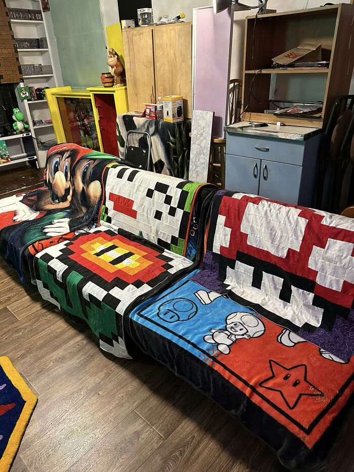 Couches covered with retro gaming blankets featuring pixel art and characters in a nostalgic gaming-themed room.
