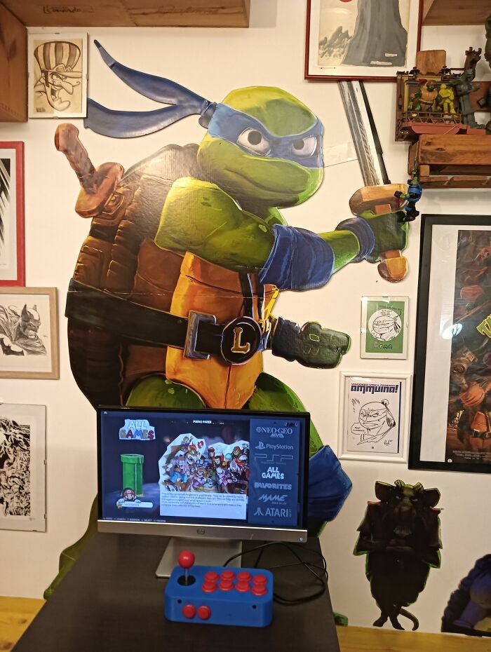 Large Teenage Mutant Ninja Turtle wall art with retro gaming setup including joystick and classic game menu on screen.