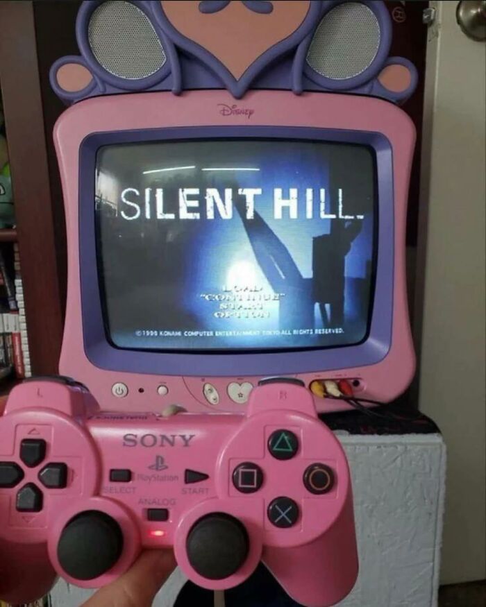 Pink retro gaming TV with Silent Hill game on screen and pink Sony PlayStation controller held in front.
