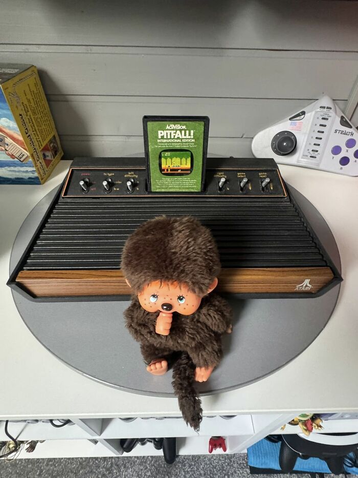 Atari console with Pitfall game cartridge and a vintage plush toy displayed for retro gaming and nostalgia.