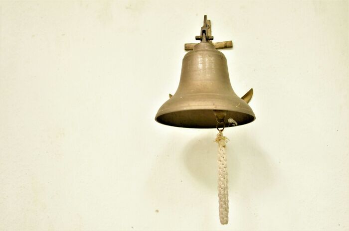 Old brass bell hanging on a plain wall, evoking eerie atmosphere for night shift workers paranormal encounters.