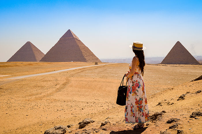 Woman in a floral dress and hat viewing the Egyptian pyramids, illustrating absurd things rich people spend money on.