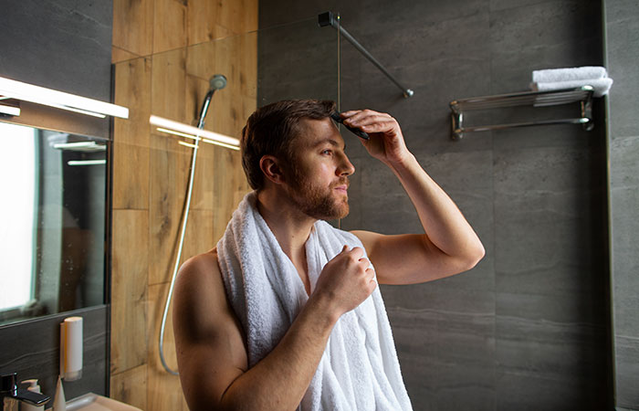 Man with towel on shoulders grooming hair in modern bathroom, illustrating absurd things rich people spend money on.