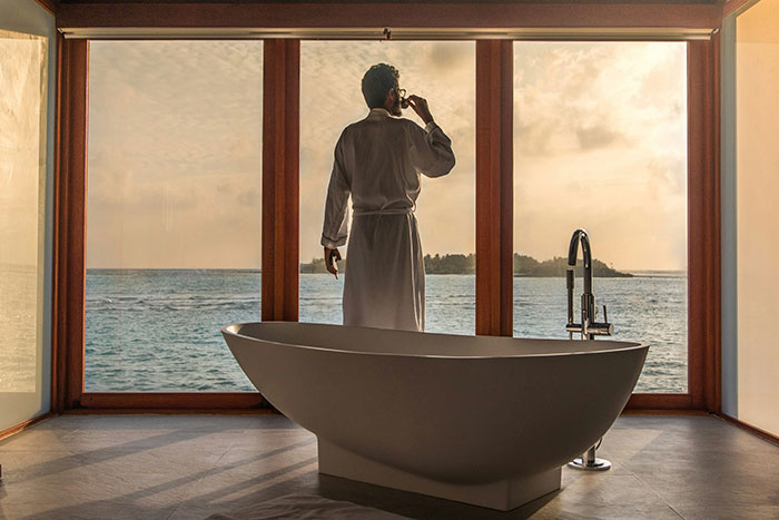 Man in bathrobe overlooking ocean view from luxury bathroom, illustrating absurd things rich people spend money on.