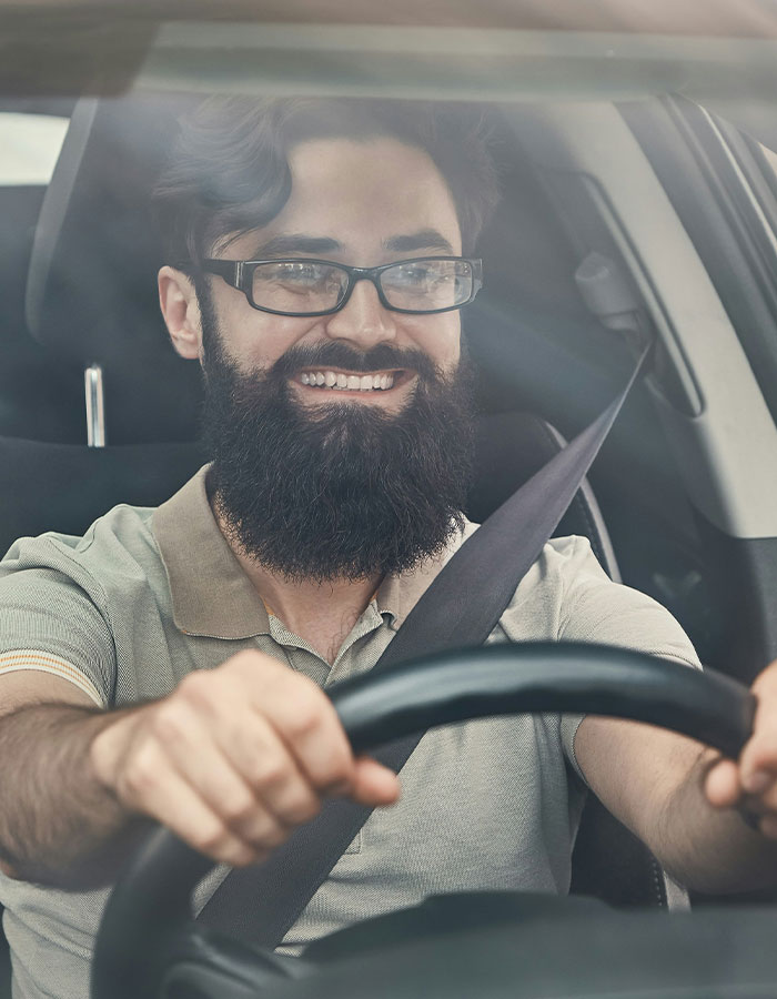 Bearded man smiling and driving a car, illustrating a road rage passenger's coffee toss backfiring hilariously.