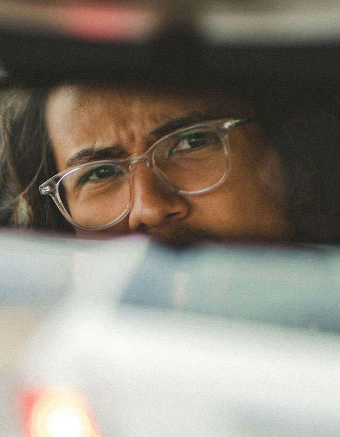 Man wearing glasses looking intensely through a car rearview mirror during a road rage moment and coffee toss incident.