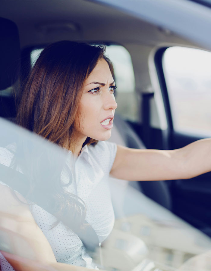 Angry woman driving a car, showing road rage, frustrated and yelling while gripping the steering wheel intensely.