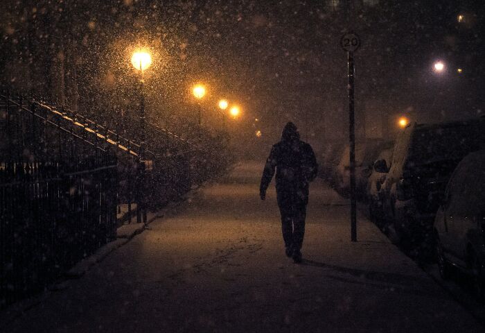Person walking alone on a snowy street at night under dim streetlights, capturing the Reddit experience not for the faint-hearted.