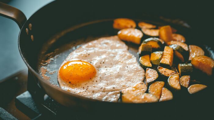 Fried egg and roasted sweet potato pieces cooking in a black pan, illustrating disturbing food facts shared by people.