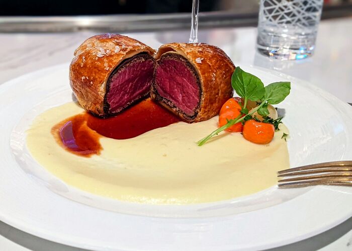 Beef Wellington with rare cooked center served with creamy mashed potatoes and glazed carrots on a white plate in a restaurant setting