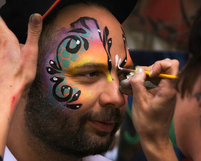 Man having colorful face paint applied with brush demonstrating a strange money-making hack.
