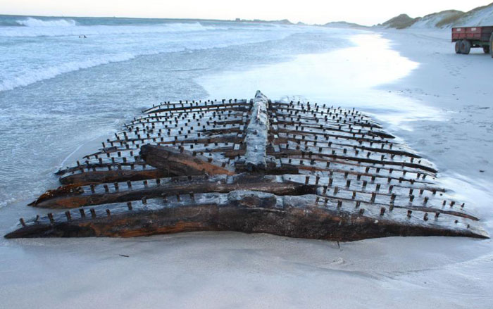 Weathered remains of Sanday ship wreck exposed on sandy beach with ocean waves in the background at low tide.