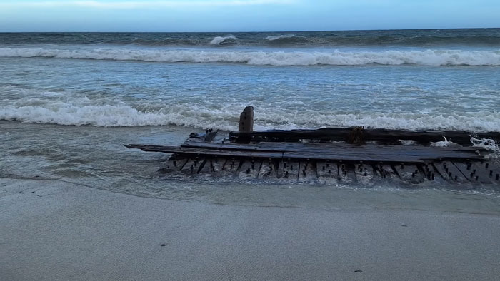 Partially buried wooden ship wreck on the sandy shore with waves gently crashing under a cloudy sky on Sanday.