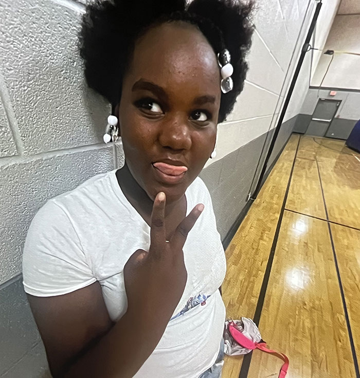 Young girl in white shirt making a peace sign in a gym, related to hospital firing 15 nurses after patient suicide.
