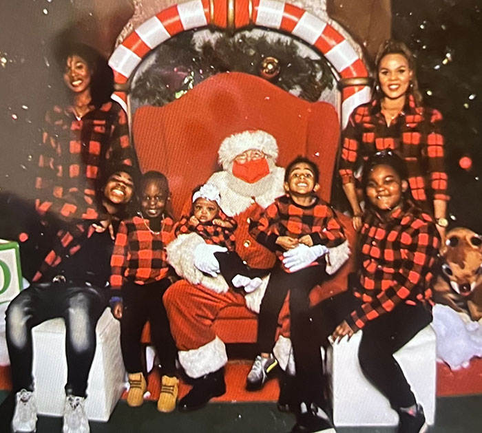 Group photo with children and adults in matching red plaid outfits sitting around Santa Claus in holiday setting, hospital nurses fired.