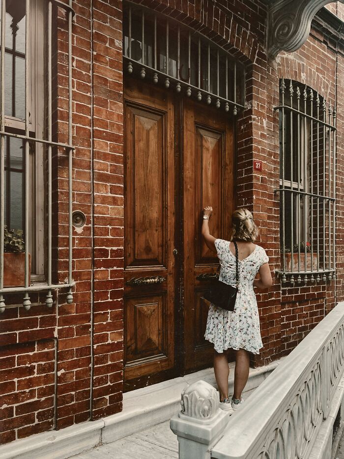 Woman in floral dress knocking on a large wooden door of a brick building representing scams that fool a millennial.