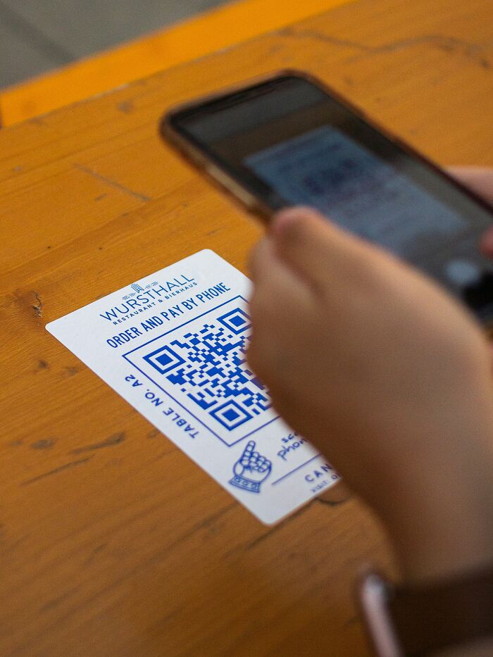 Person scanning QR code on phone at a restaurant highlighting common scams that fool millennials in digital payments.