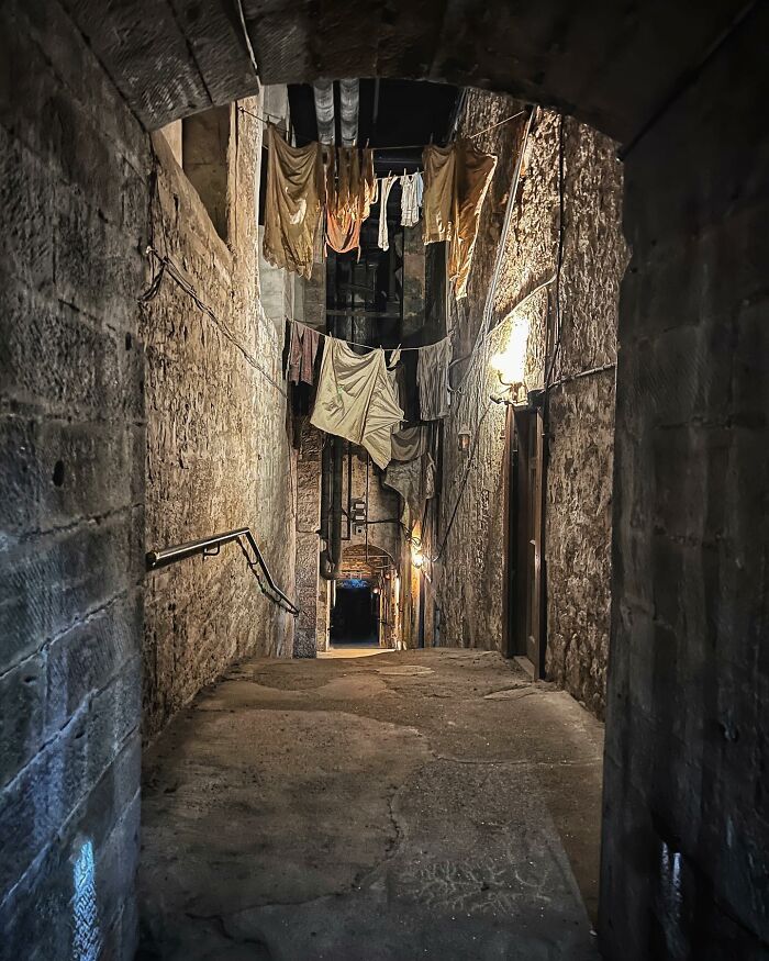 Narrow, dimly lit stone alley with old hanging clothes, representing an eerie abandoned place atmosphere at night.