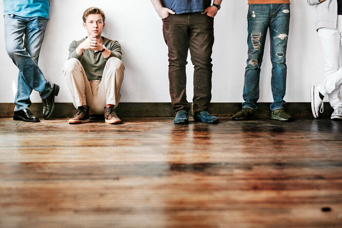 Group of young men showing alpha vibe traits, one sitting on floor while others stand against white wall. - 6