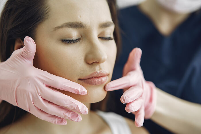 Close-up of a woman receiving facial treatment from a professional wearing pink gloves showing alpha vibe traits concept. - 13