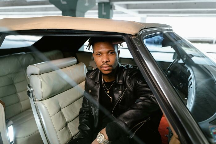 Man wearing a leather jacket sits in a vintage car, showcasing traits associated with the alpha vibe and confidence. - 19