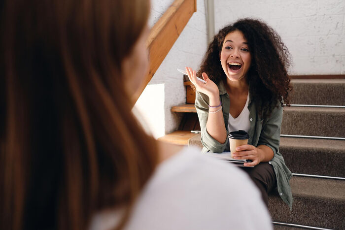 Young woman showing confident alpha vibe while laughing and holding coffee, engaging in lively conversation on stairs. - 24