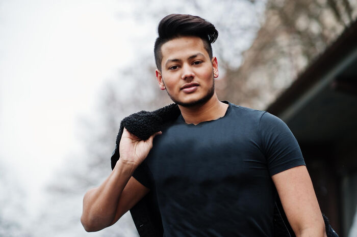 Young man with styled hair wearing a black shirt and jacket over his shoulder, embodying alpha vibe traits outdoors. - 30