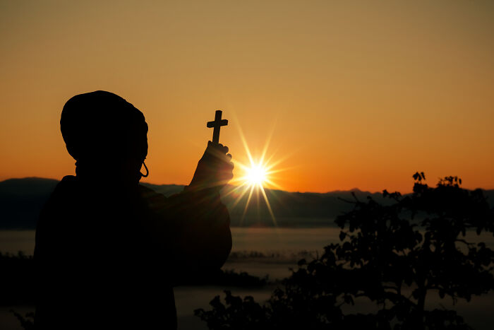 Silhouette of a person holding a cross against a sunrise, illustrating the whole alpha vibe and overcompensating traits concept. - 17
