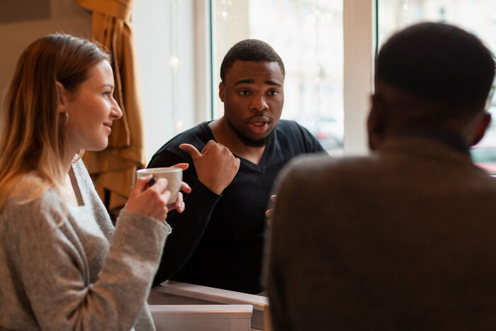 Three people having a serious conversation in a cafe, illustrating traits of overcompensating folks with an alpha vibe. - 14