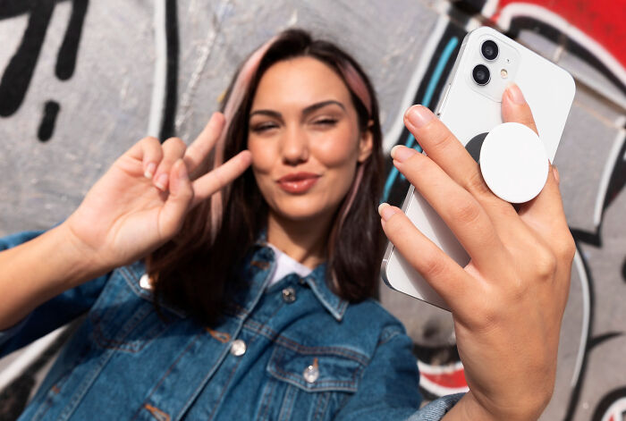 Young woman with dyed hair taking a selfie with a smartphone, showing a peace sign against a graffiti wall, capturing alpha vibe traits. - 22