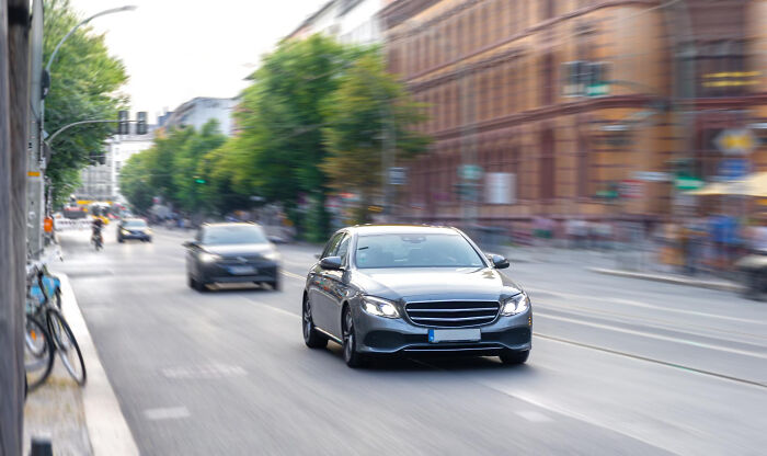 Luxury black sedan driving fast on city street, conveying the alpha vibe and overcompensating traits in urban setting. - 4