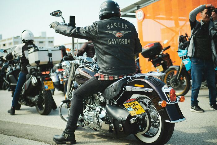 Biker in a Harley Davidson jacket on a motorcycle, embodying the alpha vibe and overcompensating traits in a group setting. - 10