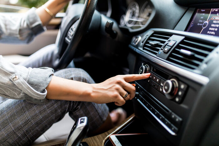 Person adjusting car radio controls inside a modern vehicle, illustrating traits of overcompensating alpha vibe behavior. - 5