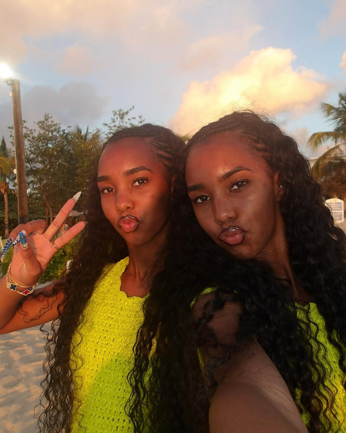 Twin daughters of Sean Diddy Combs posing together outdoors with long curly hair and bright yellow tops.