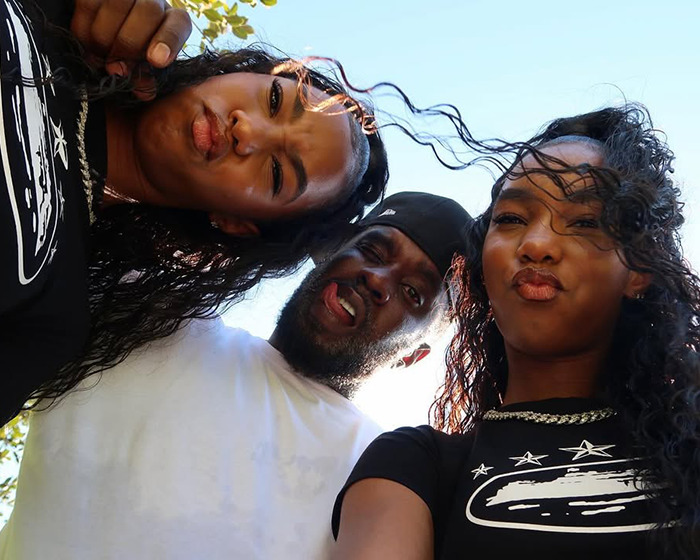 Sean Diddy Combs with his twin daughters outdoors, all making playful faces with wind blowing through their hair.