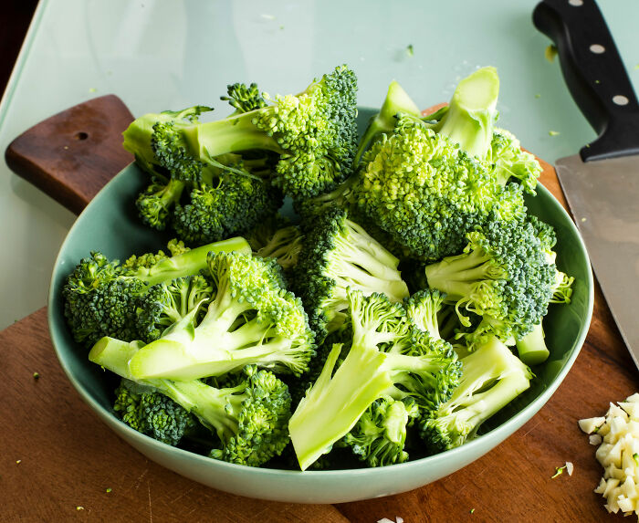 Fresh broccoli pieces in a bowl on a wooden cutting board next to a knife, related to toxic broccoli sandwich case investigation.