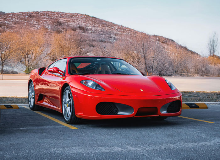 Red sports car parked in a lot with dry trees and hills in the background, symbolizing success after business collapse.
