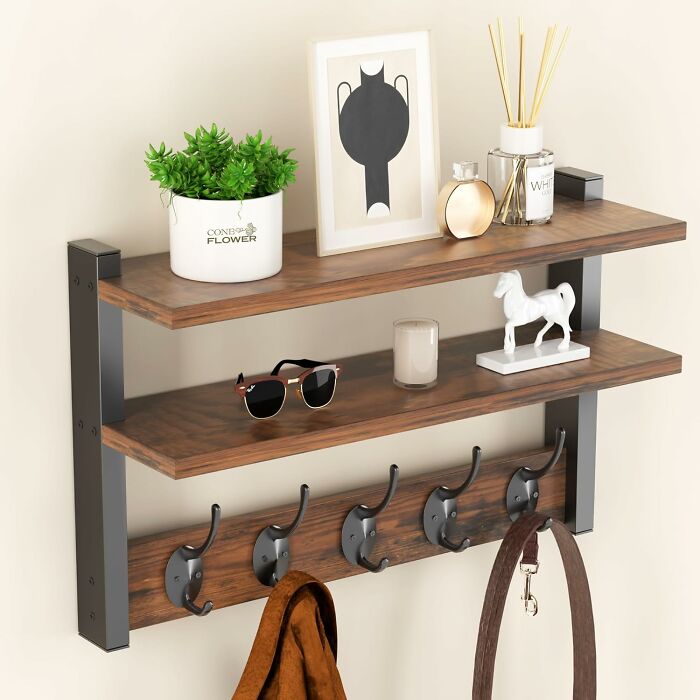 Wall-mounted wooden shelves with black metal hooks, decorated with plants, sunglasses, and small decor items, product approval.
