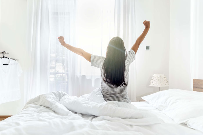 Woman stretching on bed in bright bedroom, symbolizing quick inspiration and energizing short quotes.