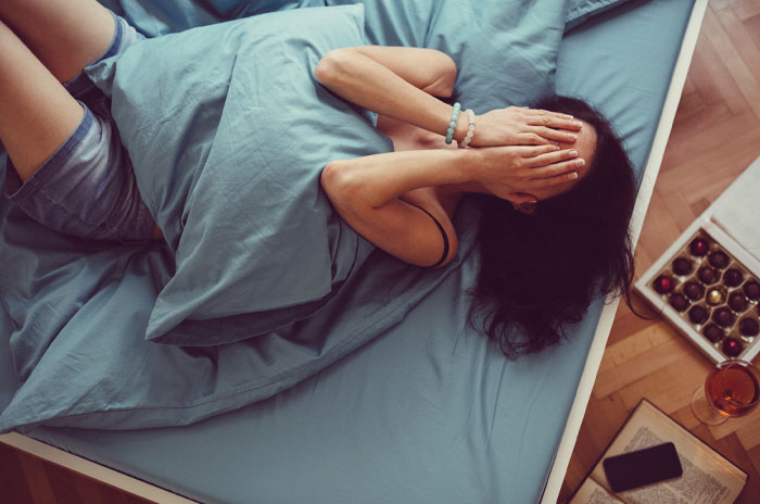 Person lying in bed with hands covering face, surrounded by cozy bedding, illustrating finding inspiration quickly.