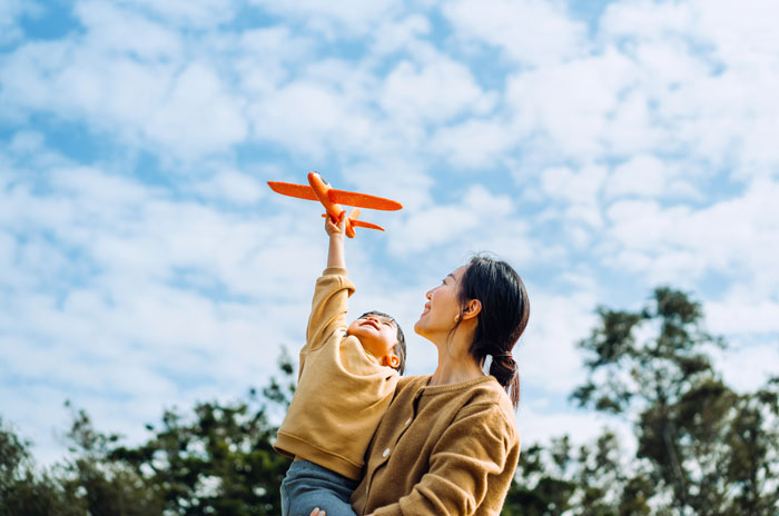 Child holding an orange toy plane with mother outdoors, symbolizing inspiration and short quotes to find motivation quickly.