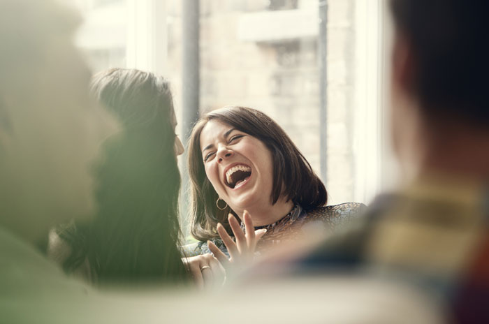 Group of friends laughing together by a window, sharing joyful moments and finding inspiration quickly with short quotes.