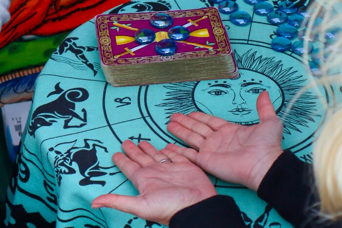 Person with open palms over zodiac cloth near tarot cards and crystal beads predicting psychic readings and experiences