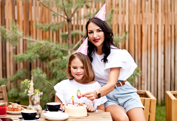 Woman and niece wearing party hats celebrating birthday with cake outdoors, highlighting spiritual awakening family conflict.