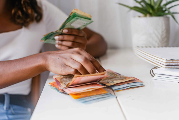 Woman counting money at table, illustrating babysitters earning a fair living wage discussion and reality check moment.