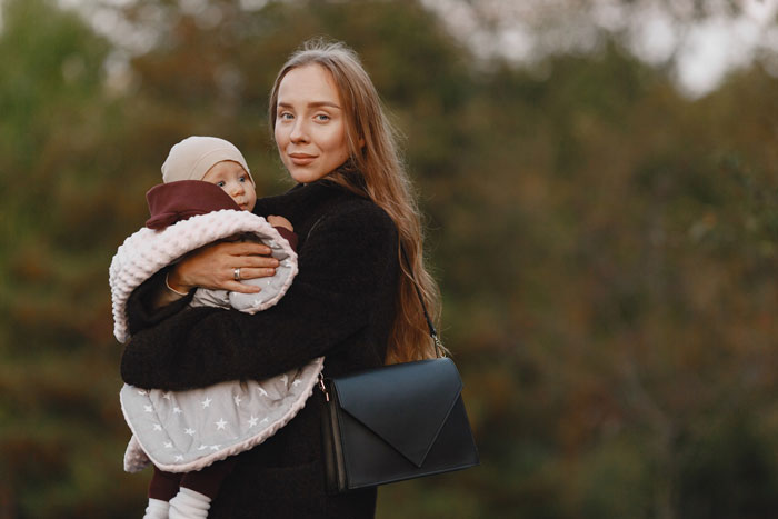 Young woman holding a baby outdoors, portraying a 19-year-old basically raising sister's kid and caring for her.