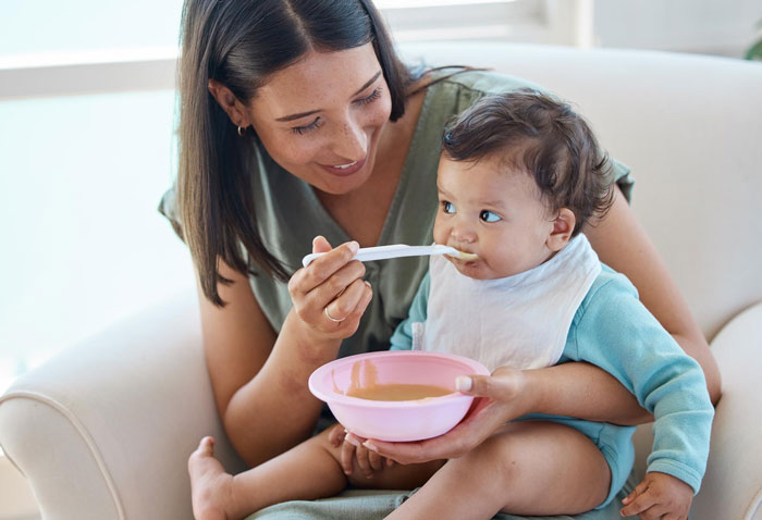 Young adult feeding toddler with a spoon, highlighting caregiving and feeding challenges in sibling responsibility.