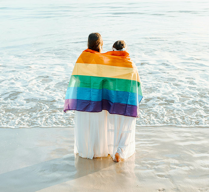 Two women standing on the beach wrapped in a rainbow flag symbolizing family ties and old fight with stepsister.