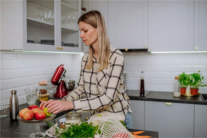 Woman in a modern kitchen arranging apples on a tray, highlighting a prank gone wrong involving a knife slipping incident.