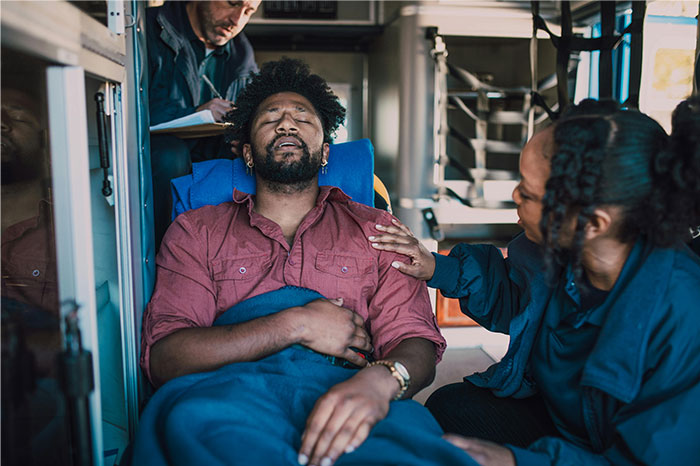 Man in pain lying on stretcher inside ambulance being comforted by woman during emergency after knife prank accident